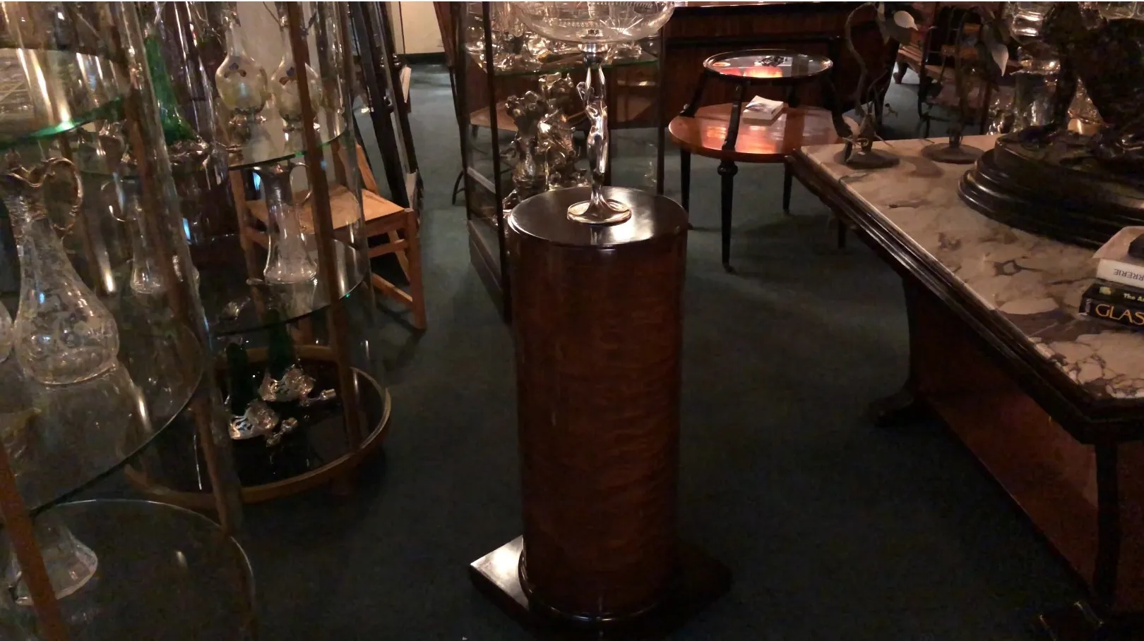 Dekorative antike Säule mit breiter Basis und komplizierten Details, umgeben von Antiquitäten.