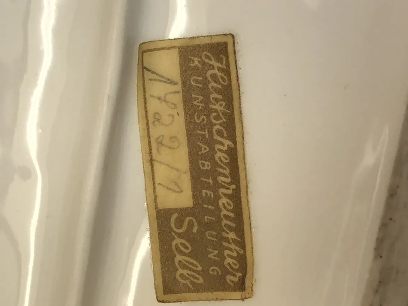 Cerámica blanca antigua con etiqueta descriptiva visible.