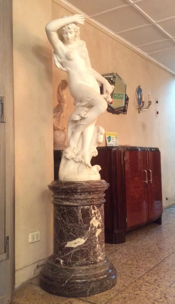 Antigua escultura sobre pedestal en ambiente clásico.