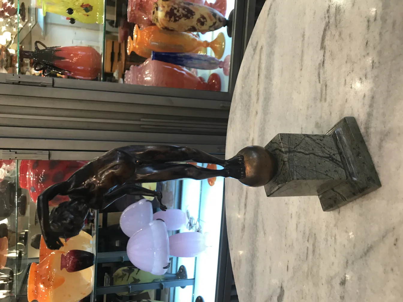 sculpture antique représentant une figure humaine élancée, décorations en verre à l'arrière-plan