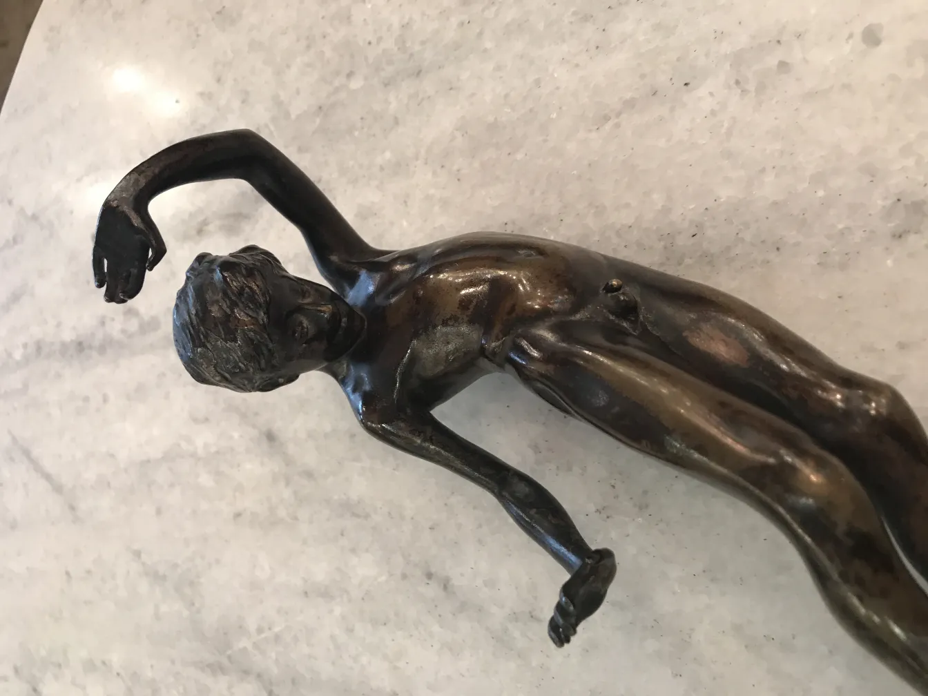 Escultura antiga de figura humana com detalhes finos, fundo claro.