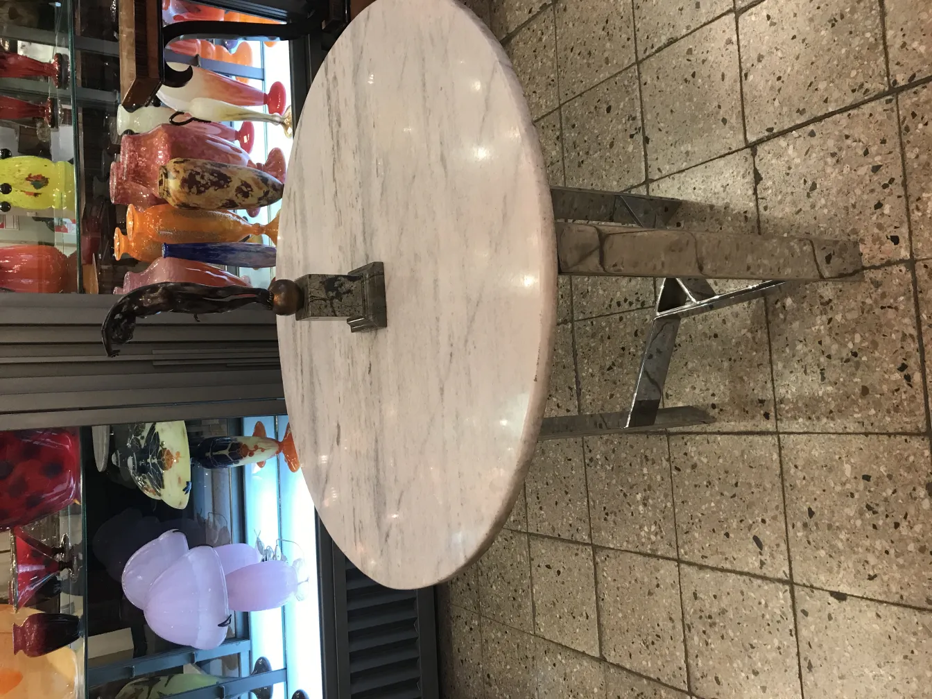 Sculpture ancienne décorative avec forme stylisée et base en métal, dans un environnement de vitrines brillantes.