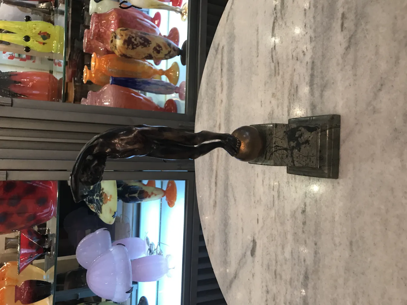 Escultura antiga de figura com base mostrando detalhes únicos e forma estilizada, cercada de objetos decorativos.