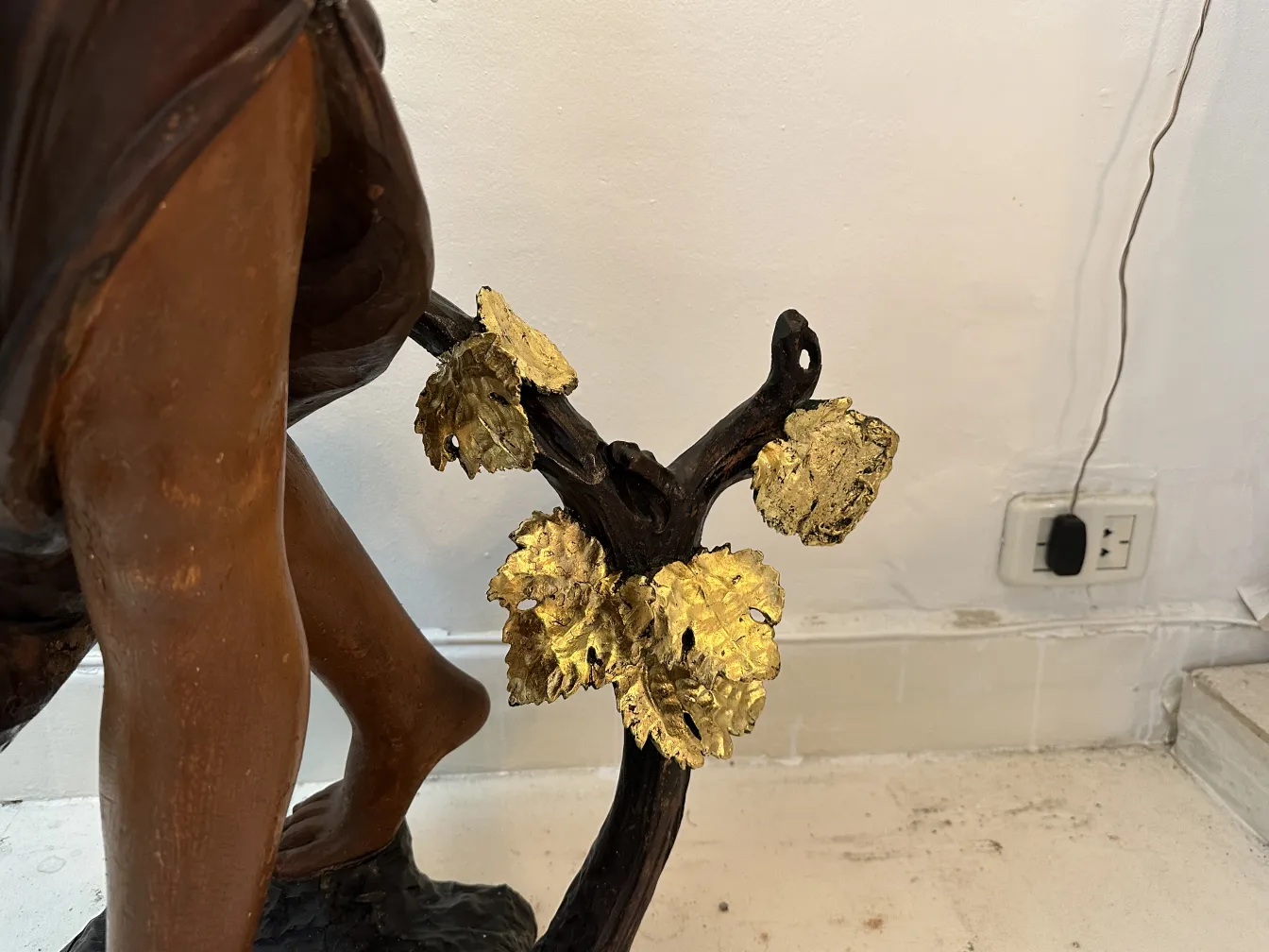 Sculpture antique d'une figure humaine avec des feuilles dorées à sa base.