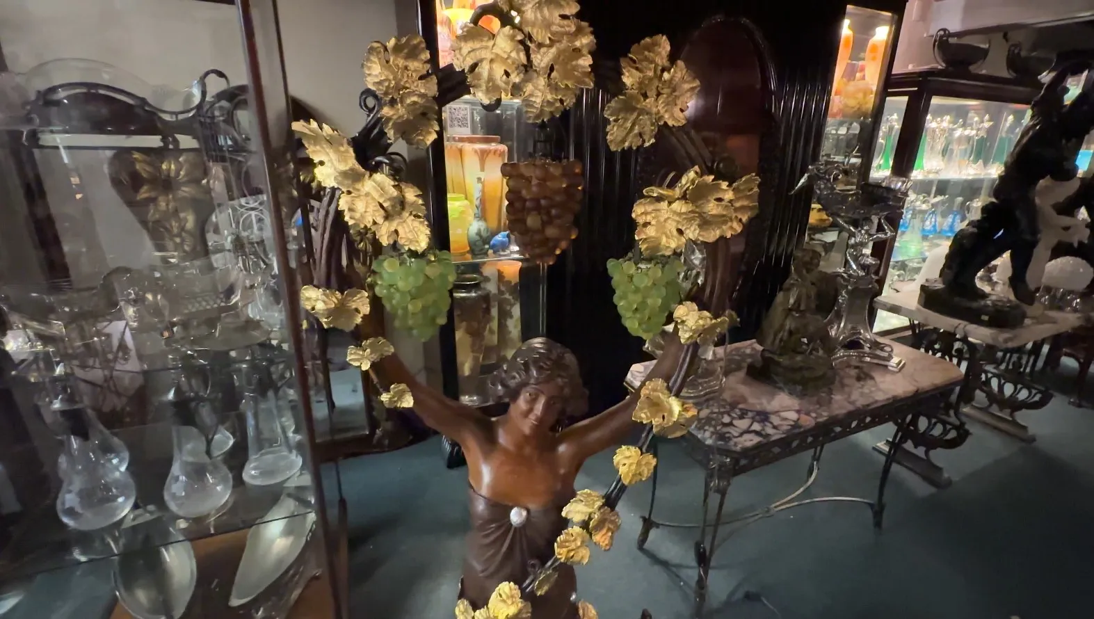 Escultura antiga de mulher adornada com folhas e uvas, ambientada em um ambiente elegante com outros objetos decorativos