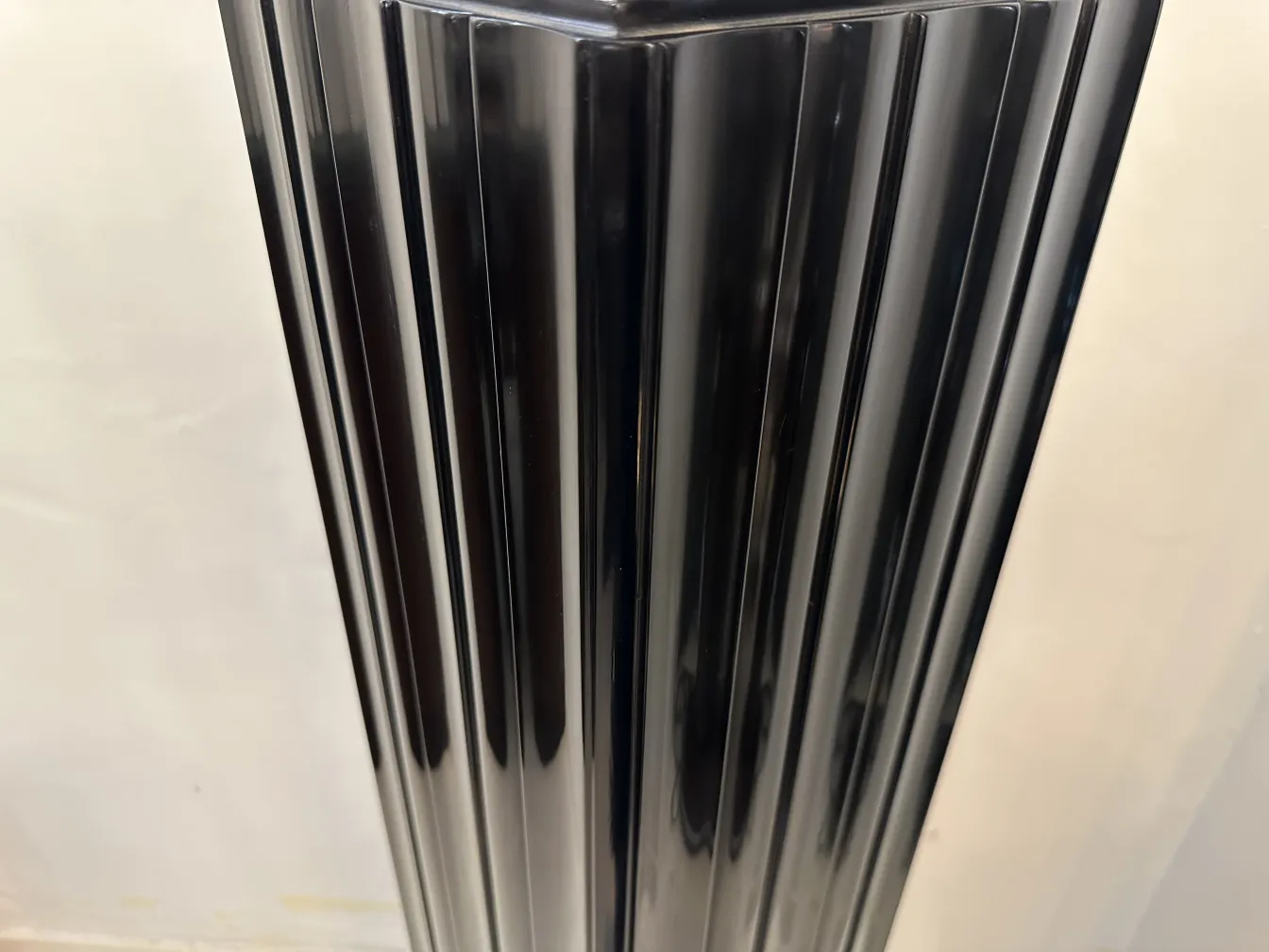 Columna antigua de color negro con diseño moderno, elegantemente tallada, situada en un fondo claro.