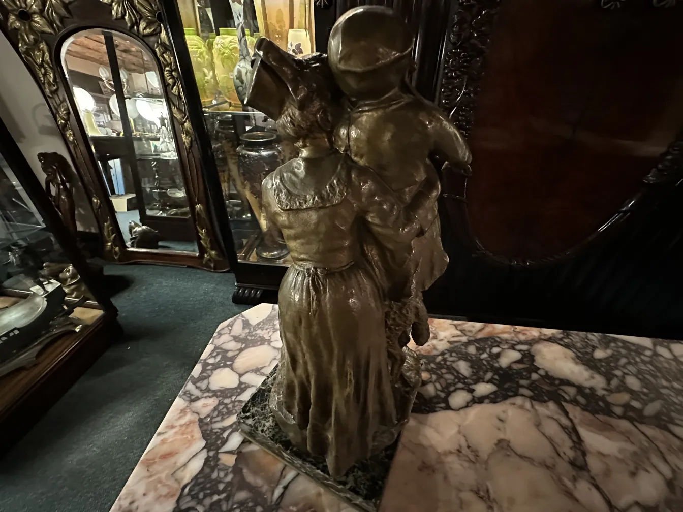 escultura antigua de mujer sosteniendo a un niño, detalle en bronce, fondo con vitrinas y espejos