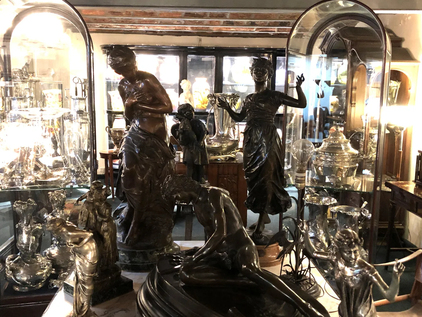 Escultura antigua figurativa en una vitrina, rodeada de piezas decorativas y antiguas.