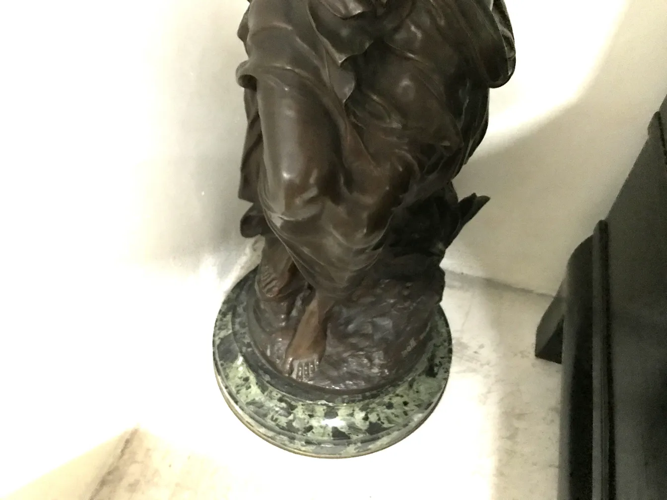 escultura antigua de un personaje con detalles decorativos y base verde