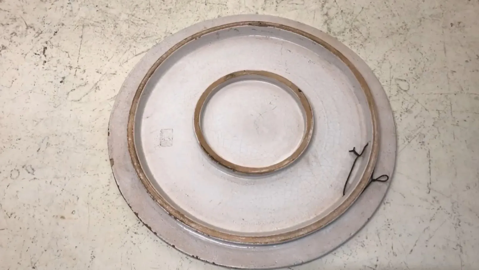 Assiette en céramique antique avec des détails dorés et une forme ronde sur un fond clair.