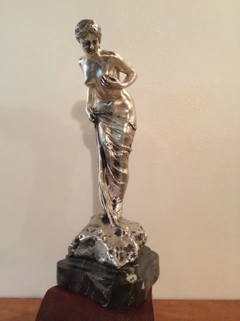 Escultura antiga de mulher com acabamento brilhante segurando uma drapeado.