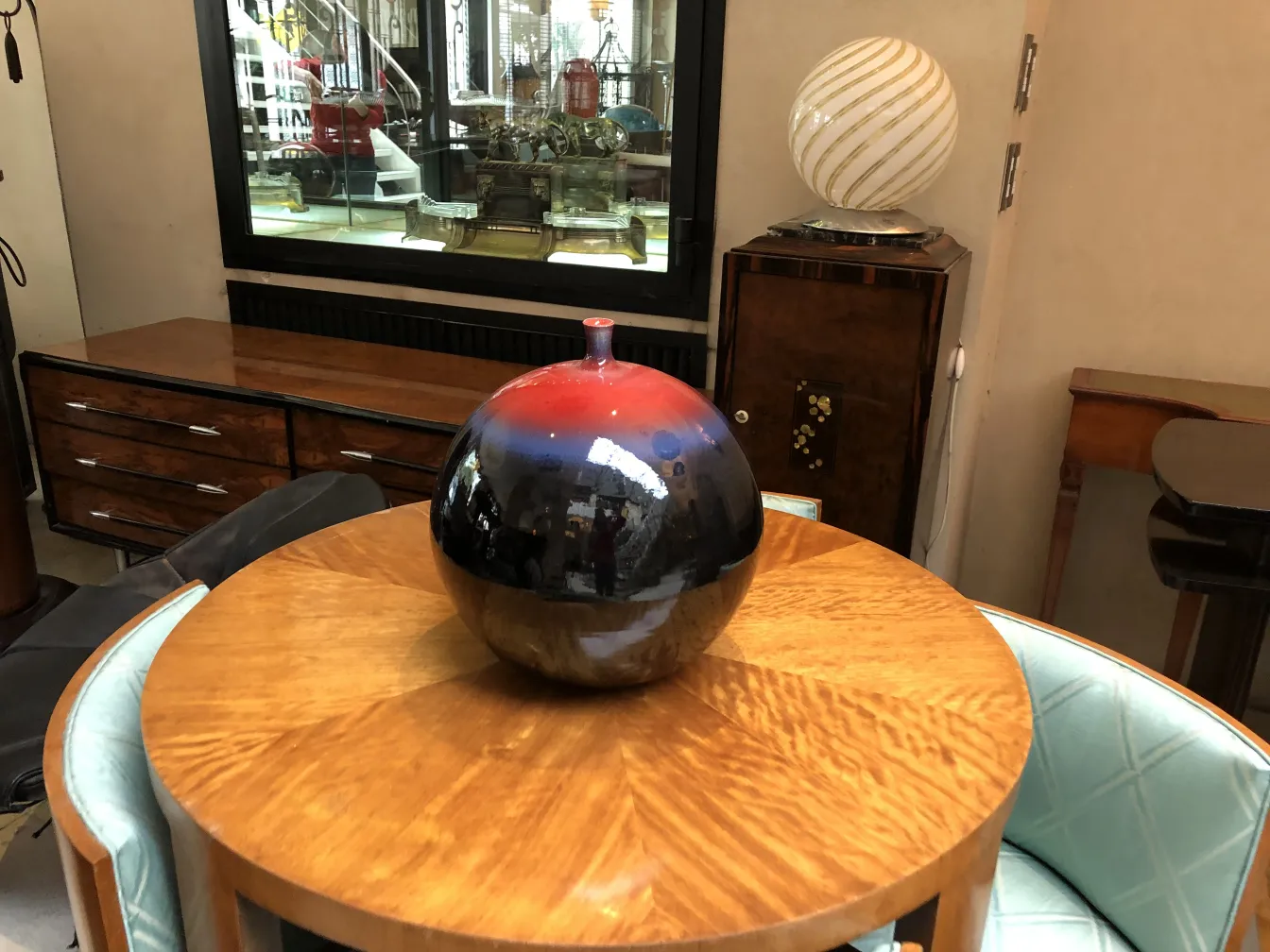 Esfera cerámica antigua decorativa, en colores negro y rojo, sobre mesa de madera.