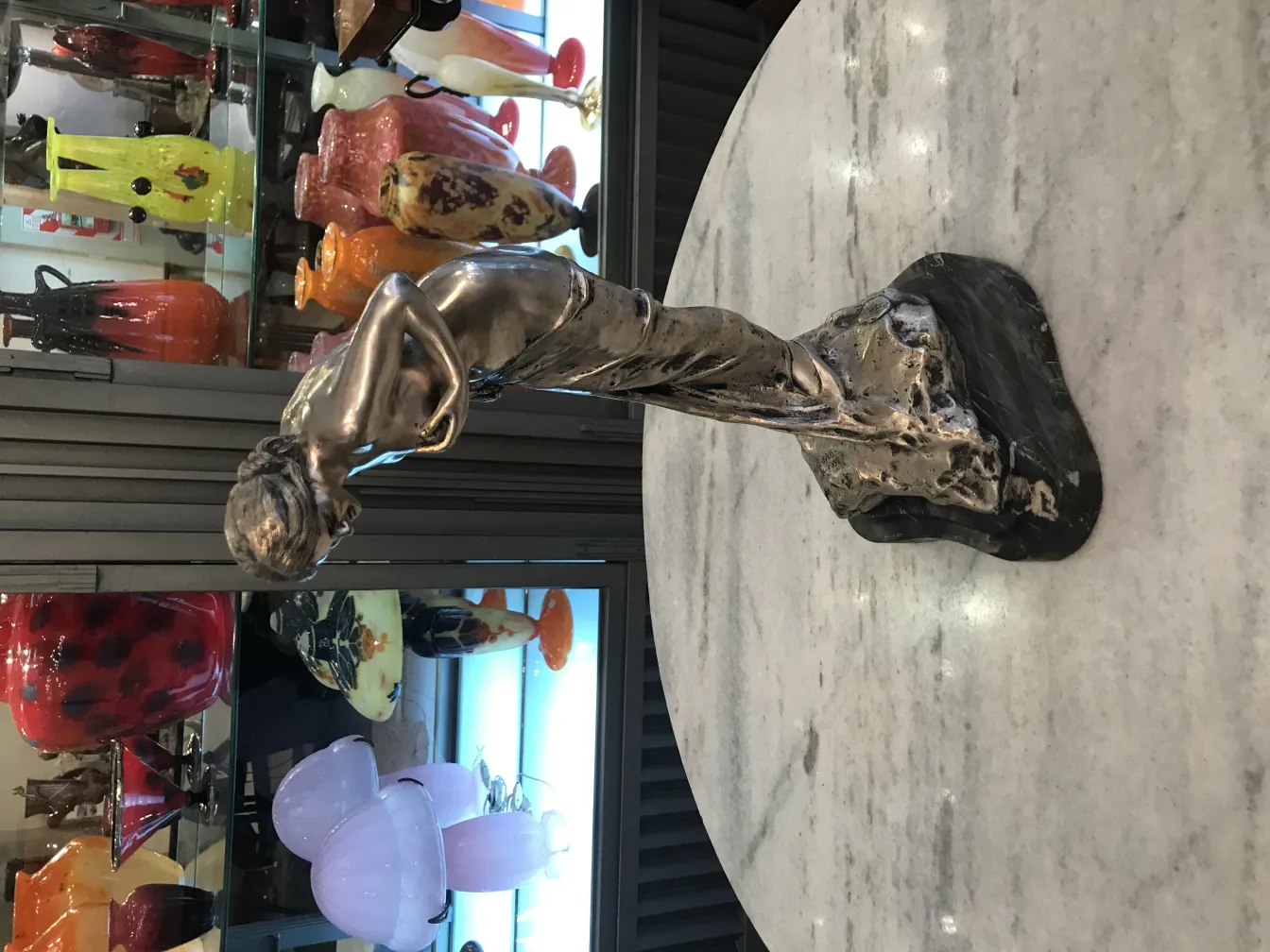 Antique sculpture of a woman in bronze, detailed and elegant against a backdrop of decorative objects.