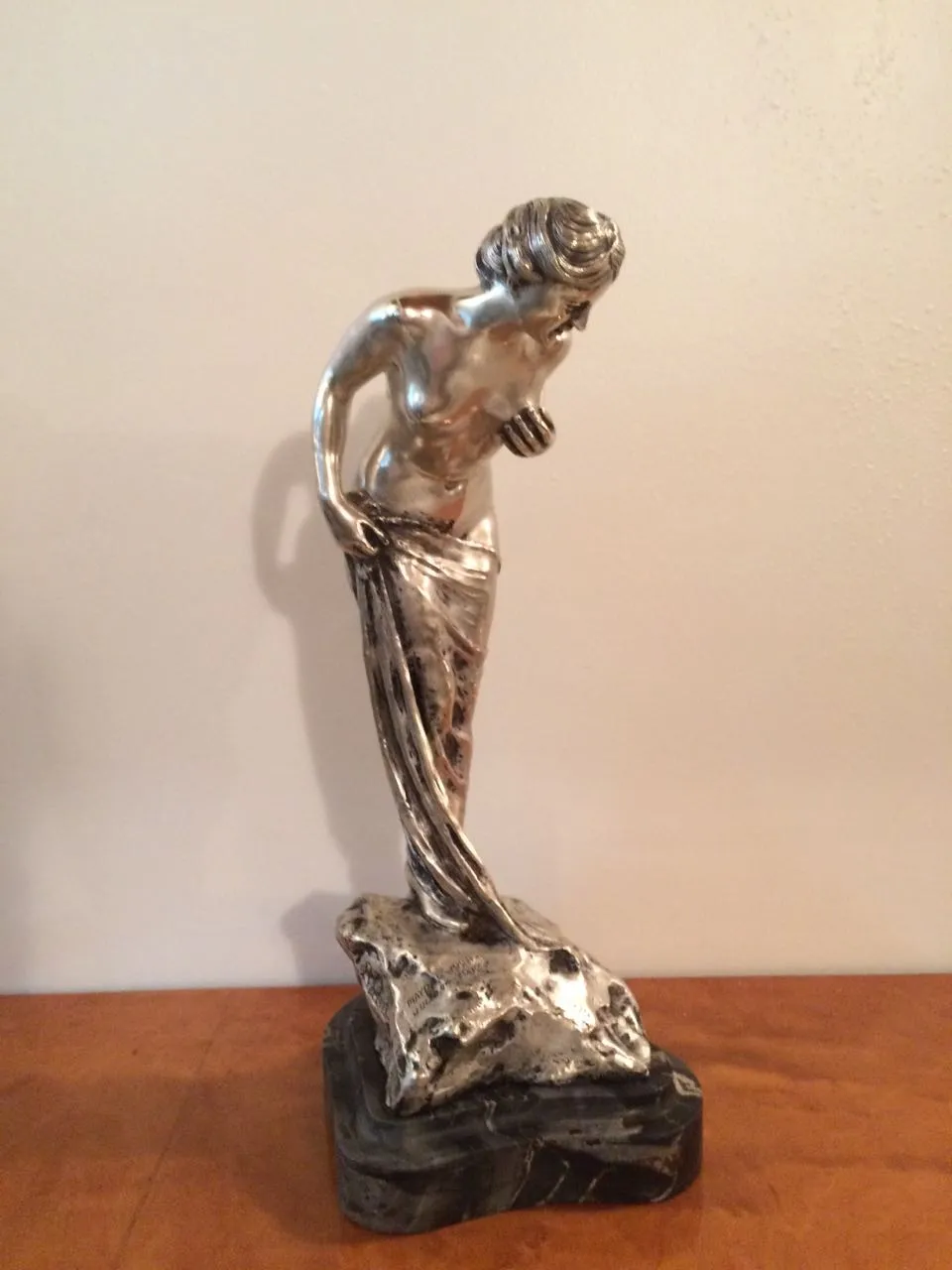 Sculpture antique d'une figure féminine élégante avec des détails brillants et une base sombre.