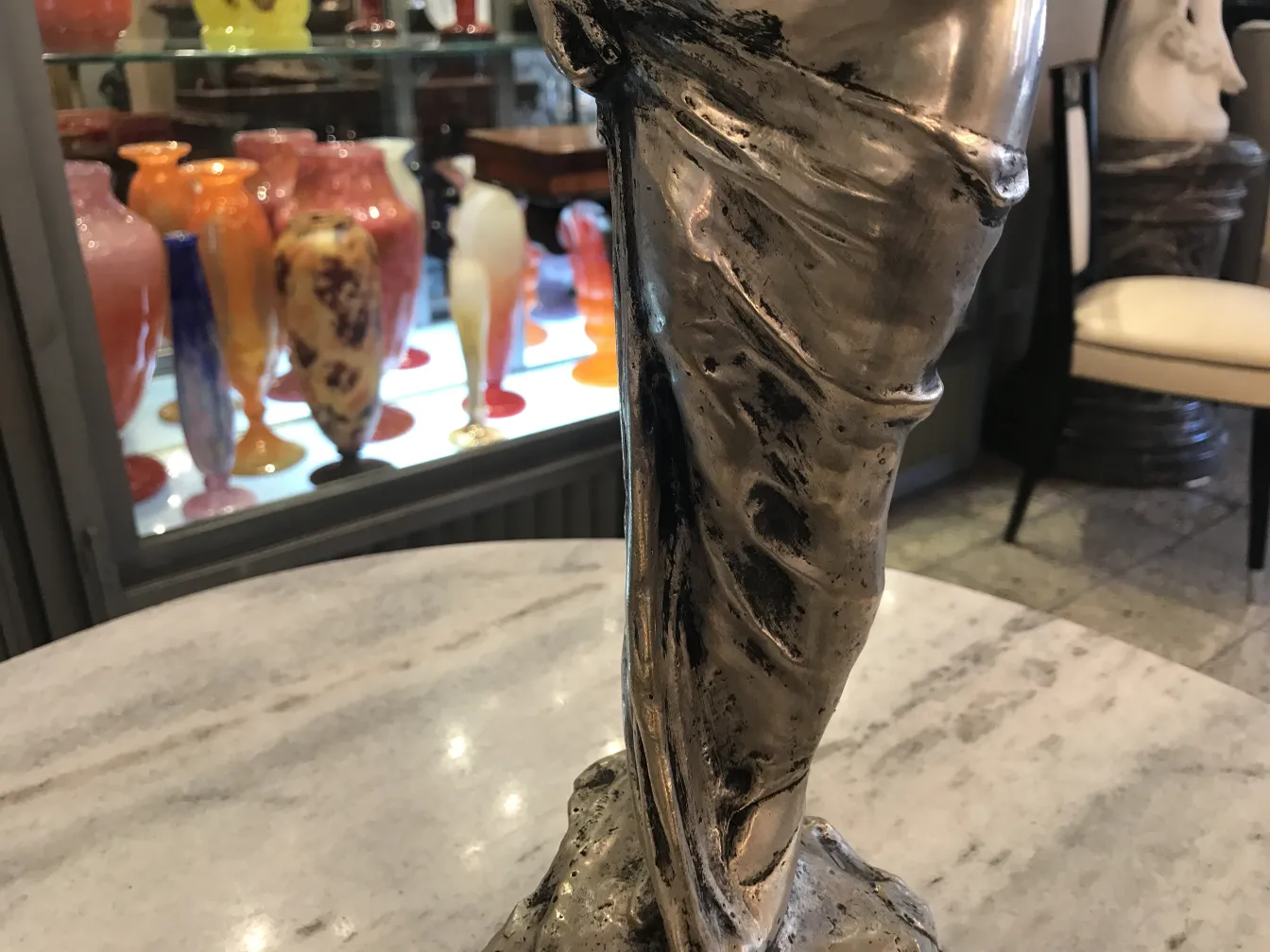 Detail of an antique sculpture with draping, surrounded by colorful glass items.