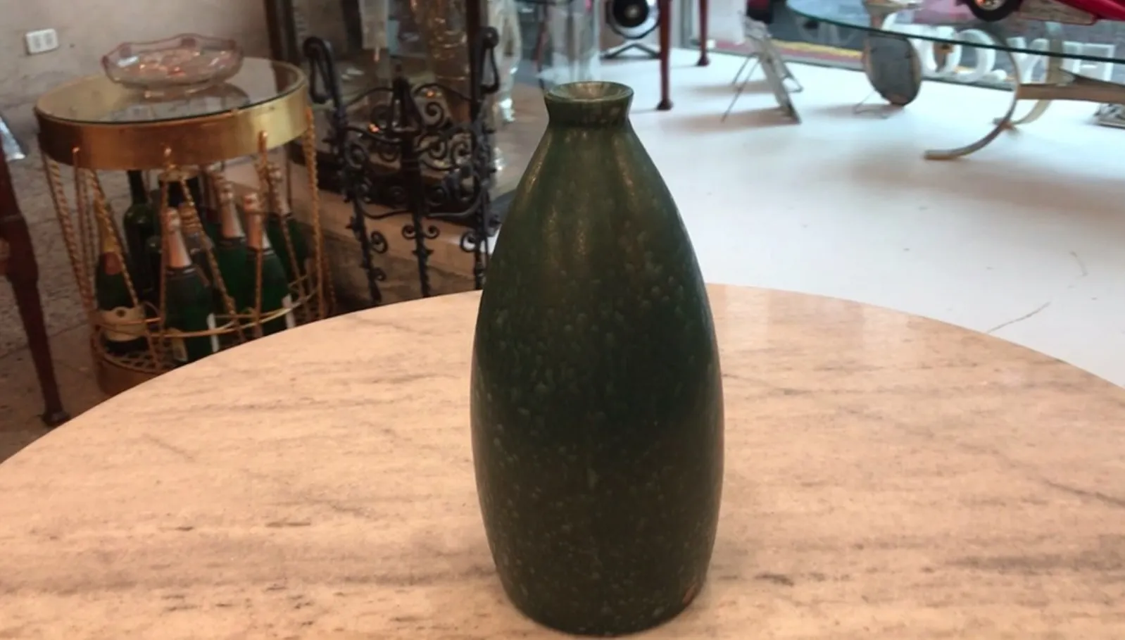 Antike grüne Keramikvase auf einem Marmortisch, umgeben von Antiquitäten.