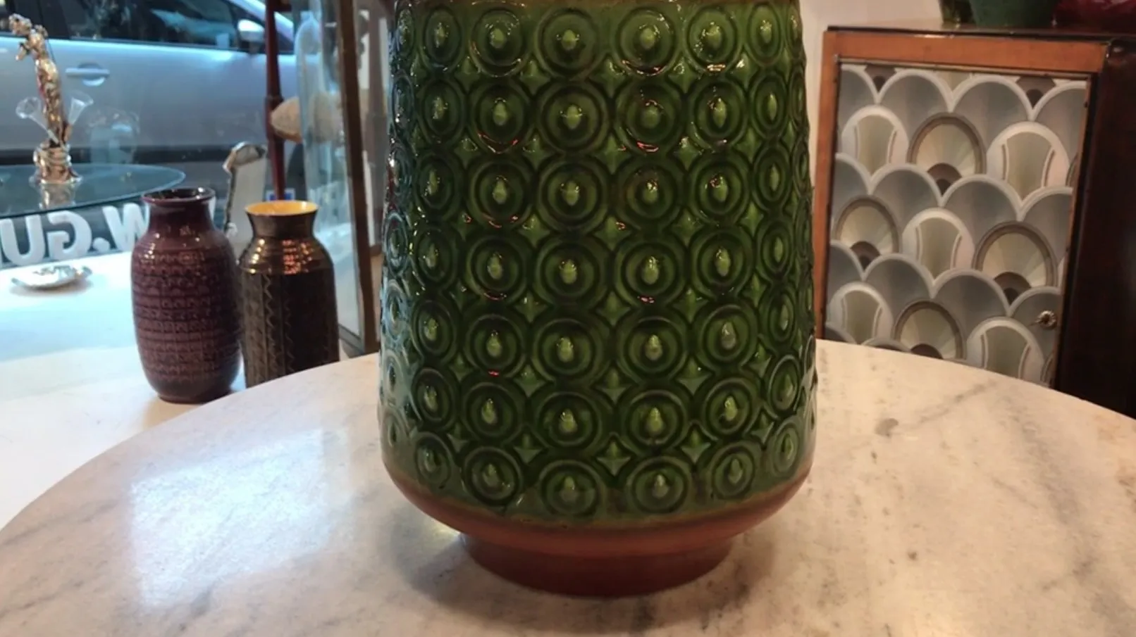 Vaso di ceramica antica verde con motivi circolari su uno sfondo avorio.