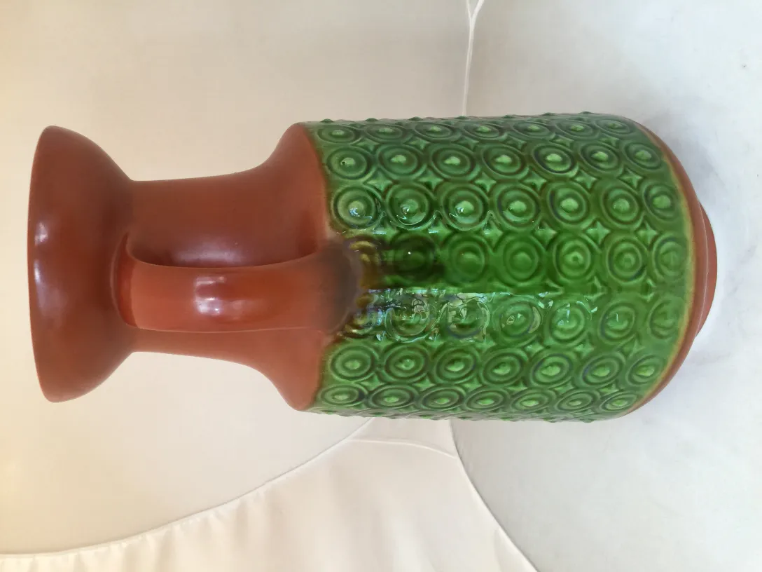 Jarrón antiguo de cerámica con diseño en verde y marrón, colocado en un fondo claro.