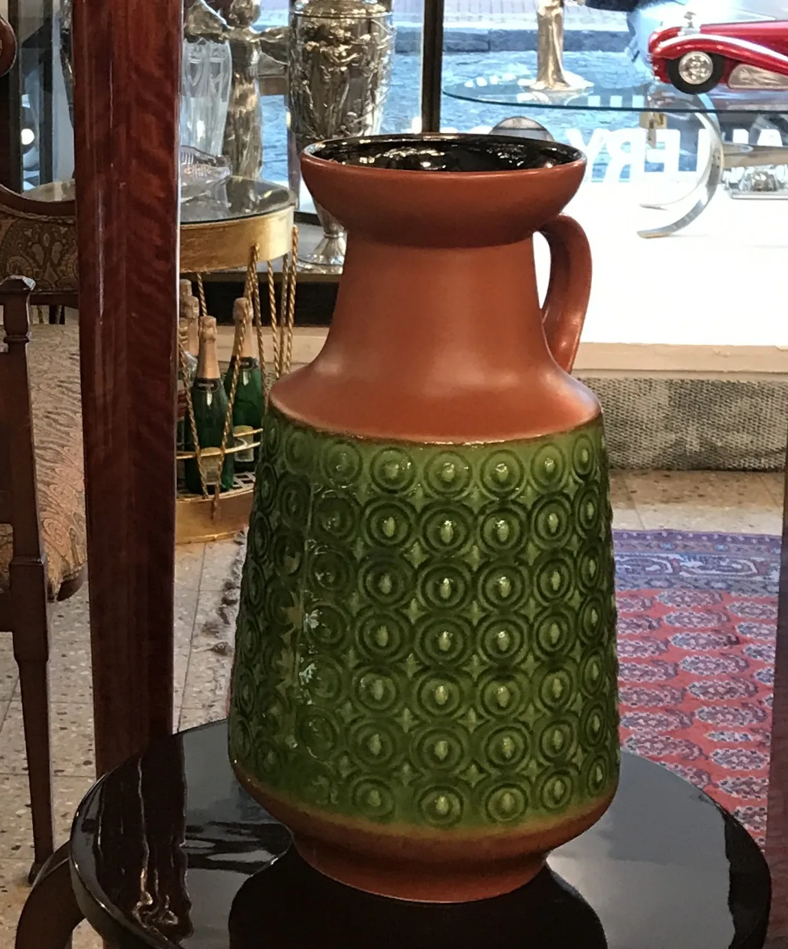 Antique green ceramic pitcher with circular decoration, surrounded by antiques.