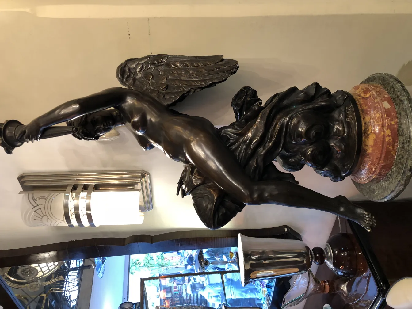 sculpture ancienne de femme avec des ailes et une lanterne, base décorative et une bouteille de bière en arrière-plan