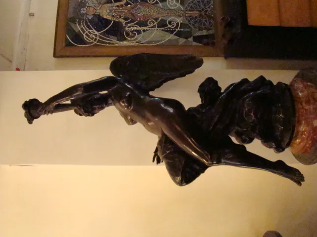 Escultura antigua con figura femenina alada y pedestal.