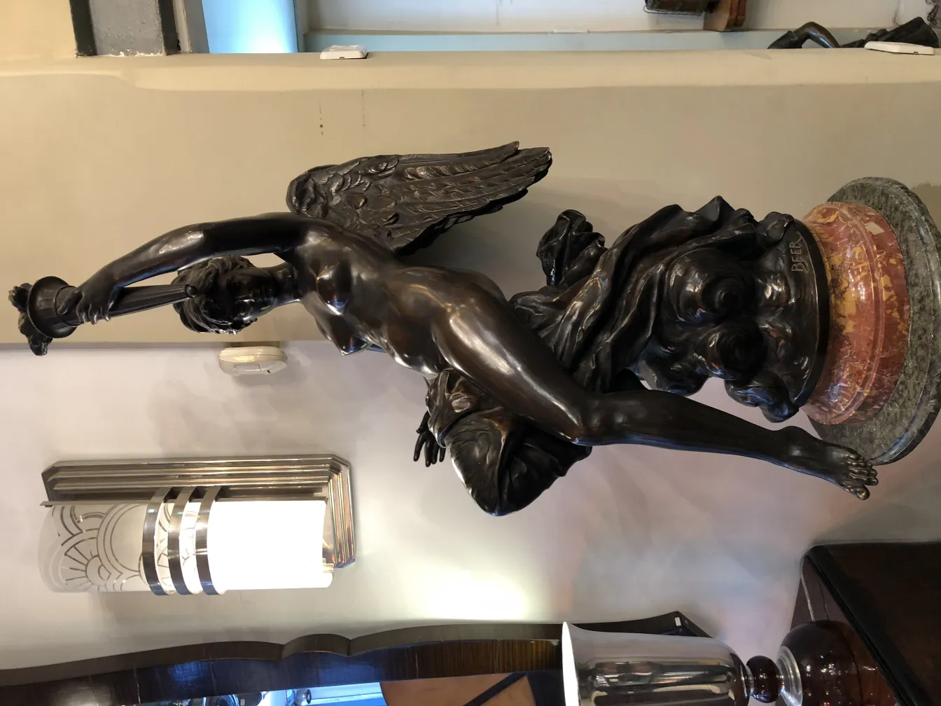 Scultura antica di figura femminile alata con base decorativa in un ambiente elegante.