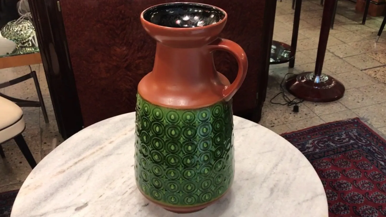 Antica giara in ceramica verde con design decorativo su un tavolo in marmo.