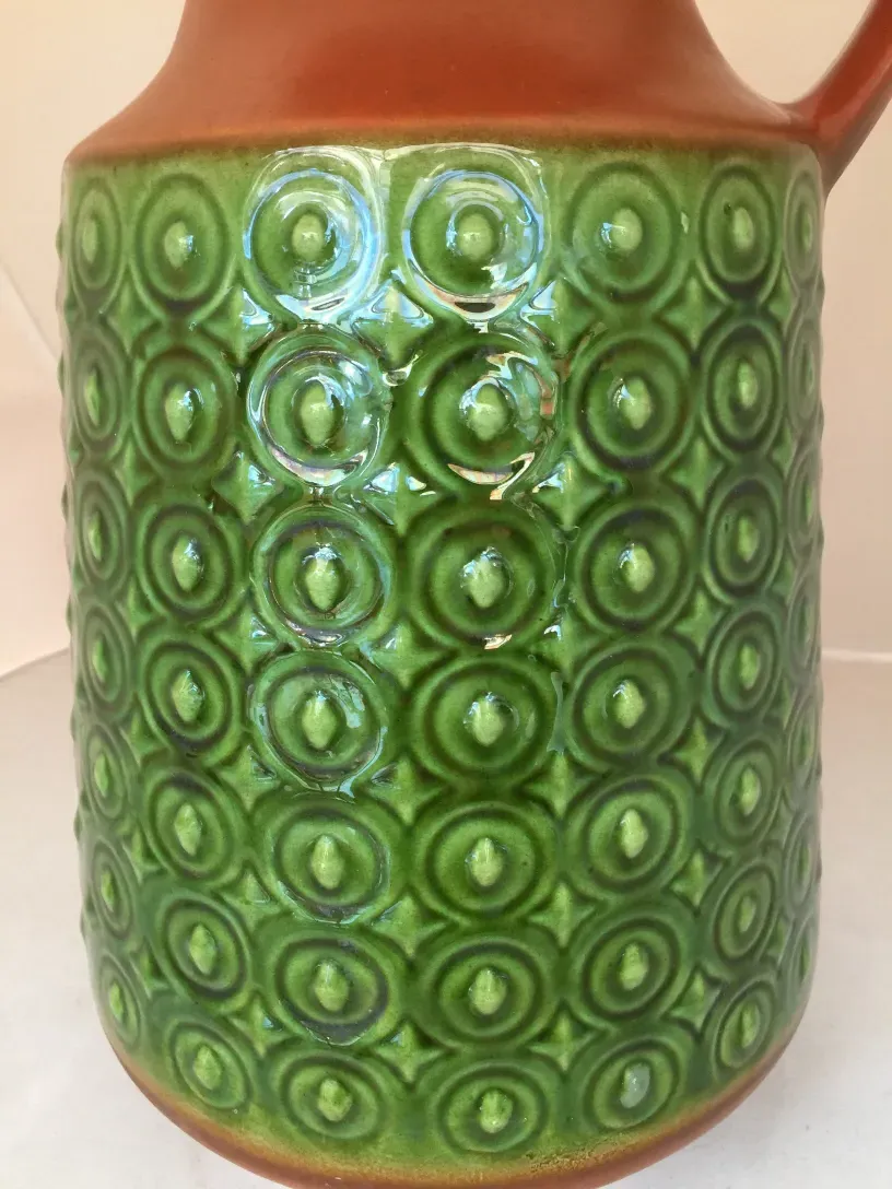 Antica brocca di ceramica verde con motivi circolari.