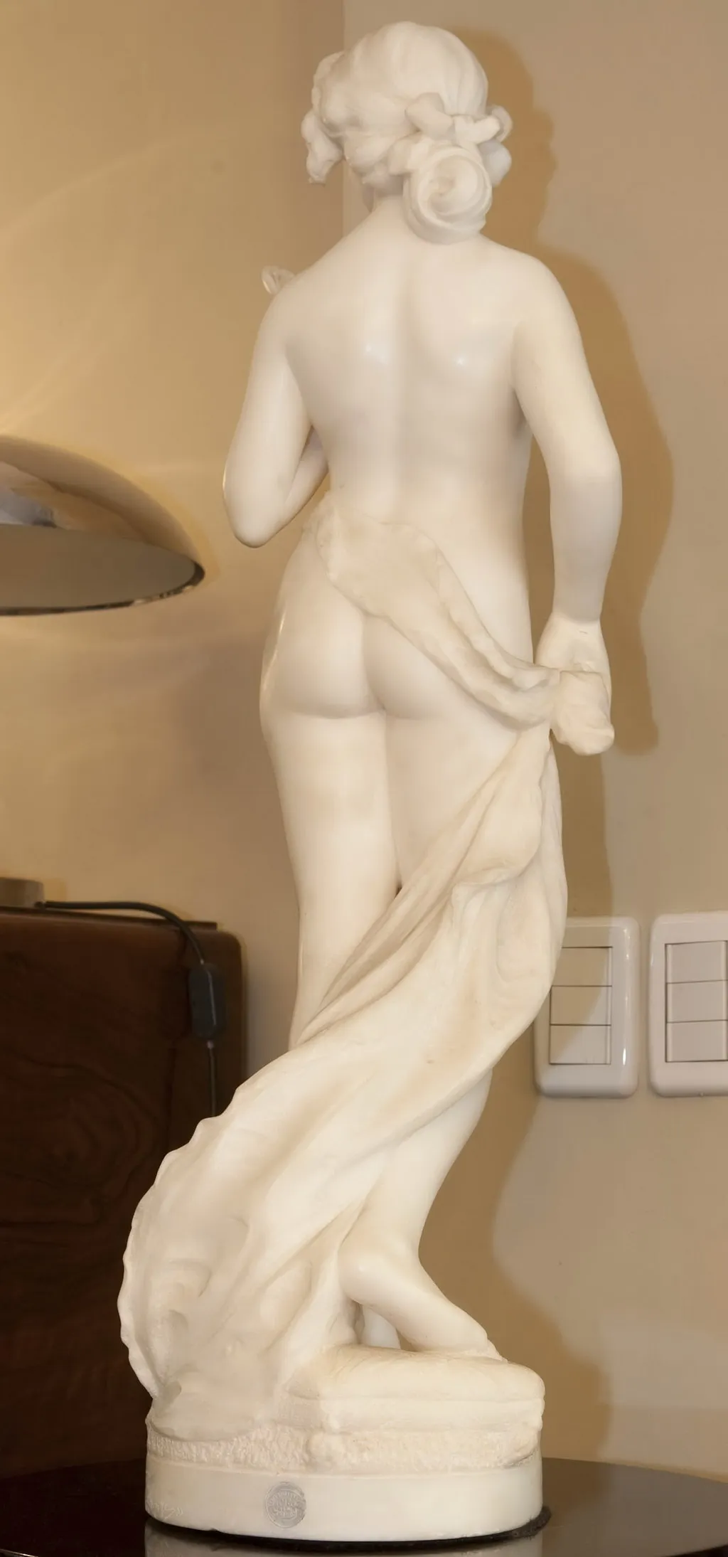 escultura antigua de una figura femenina, vista desde atrás con tela en sus manos