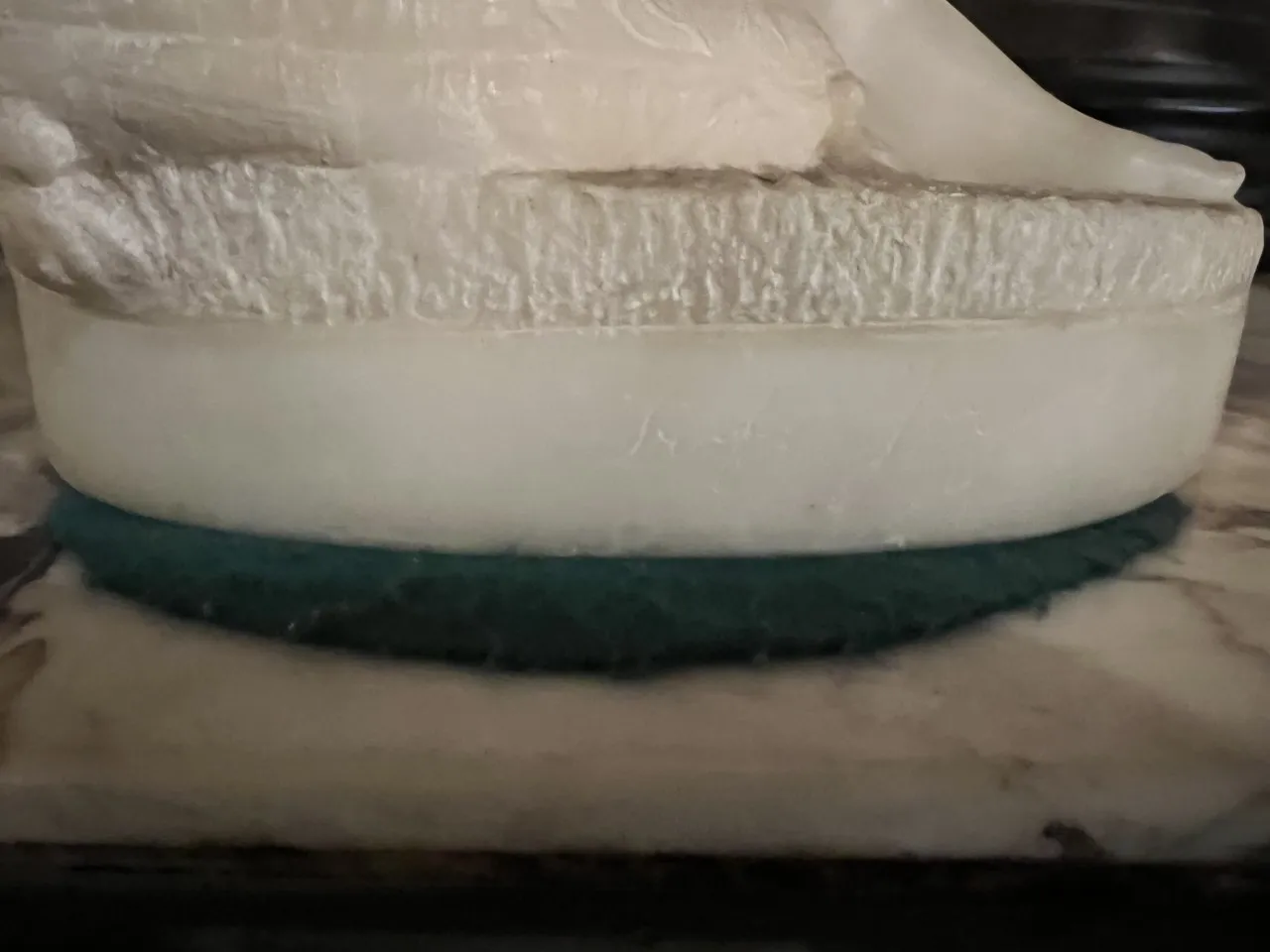 Detalhe de escultura antiga com base de mármore e tecido verde.