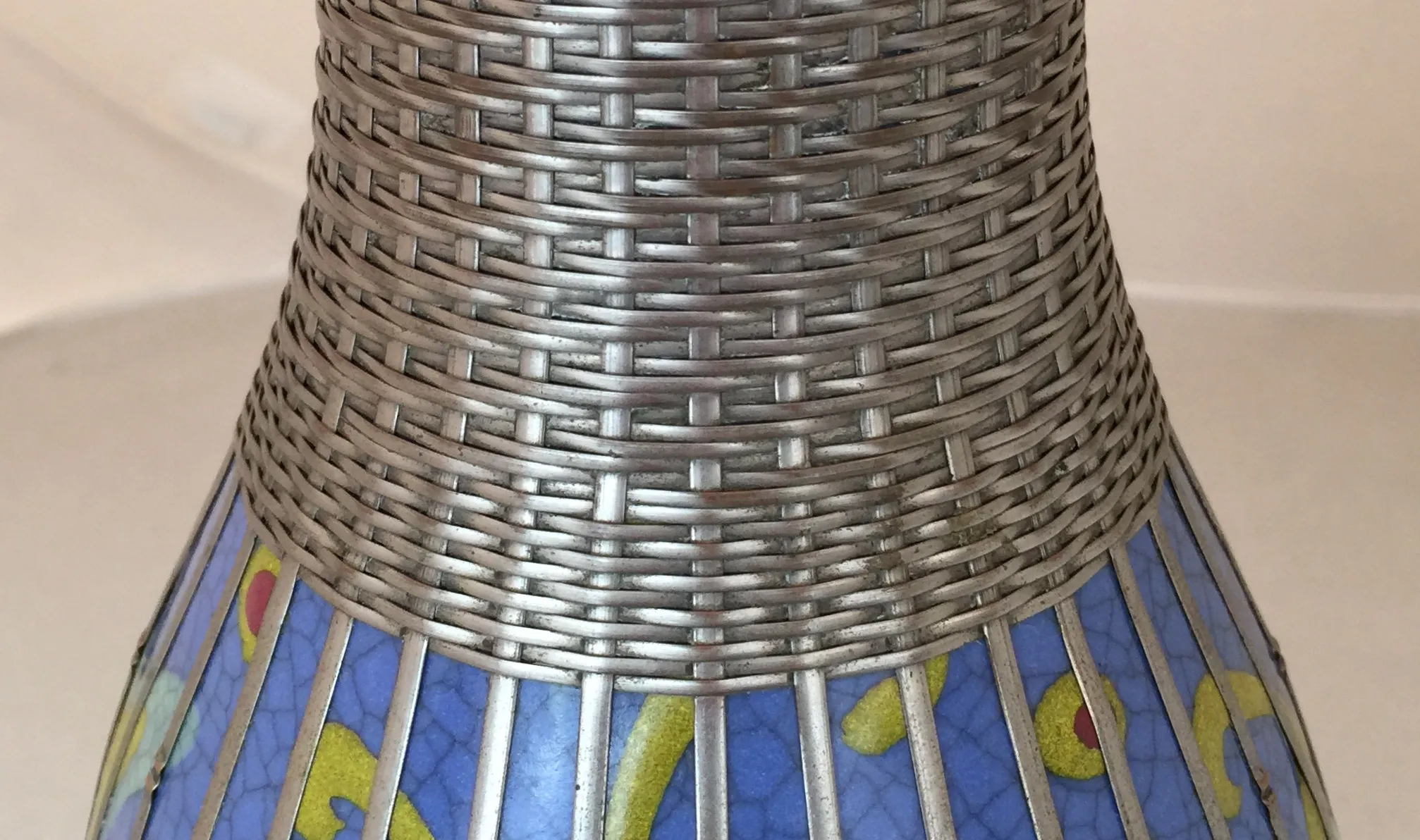 Vasija antigua de cerámica en tonos azules y amarillos, detalles tejidos decoran la parte superior.