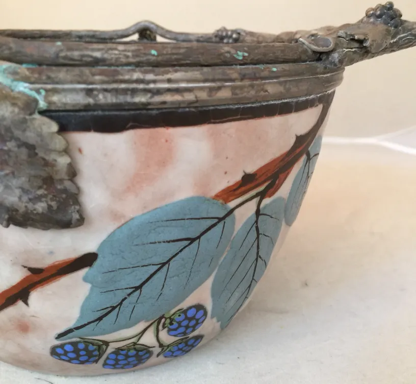 Antigua ceramica decorada con hojas verdes y bayas azules.