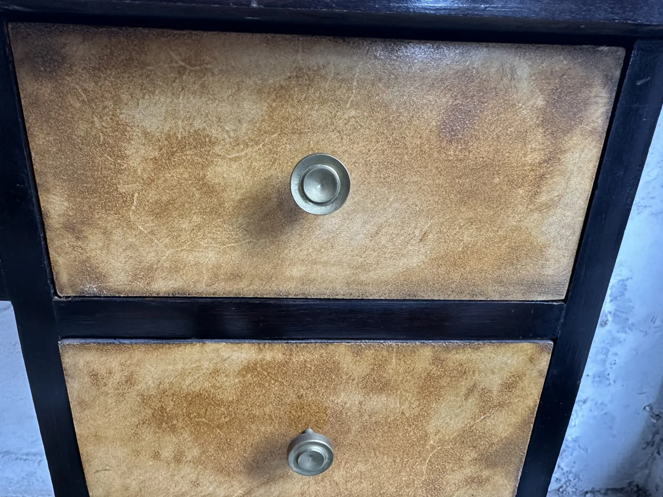 Escritorio antigo com acabamento claro e duas gavetas de bronze em um ambiente neutro.