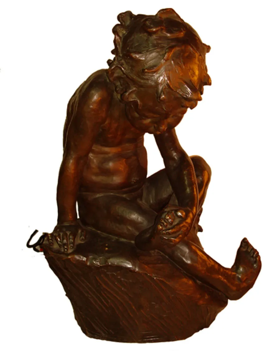 Escultura antigua de un niño sentado, expresando concentración, en un entorno sobrio.