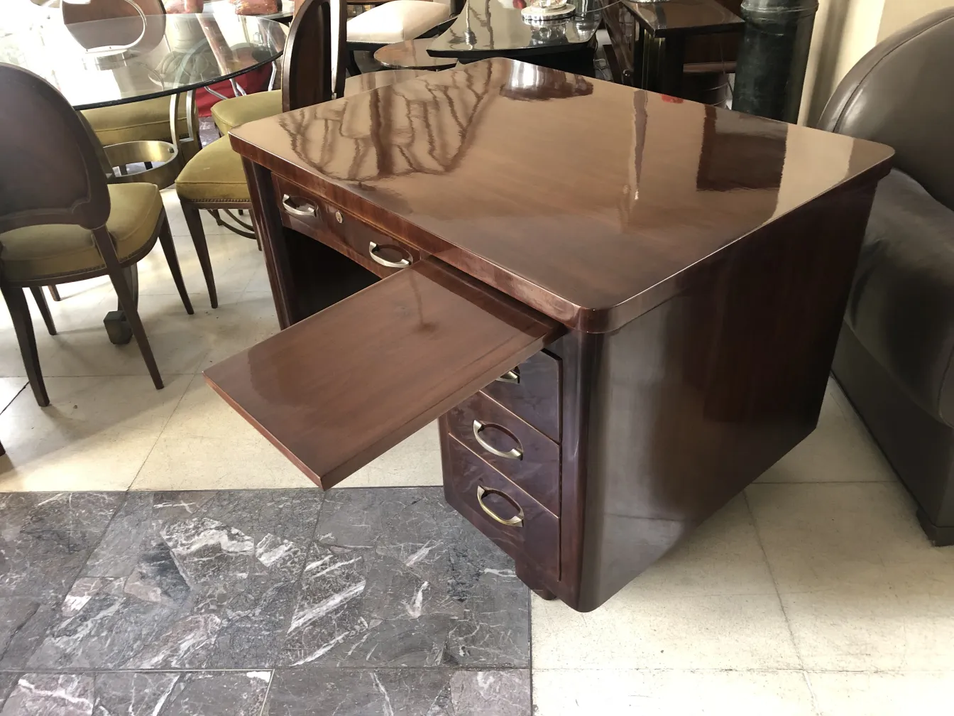 Bureau ancien avec un dessus brillant et un tiroir ouvert, entouré de chaises et d'une table.