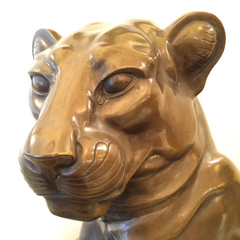 Escultura antiga em forma de cabeça de leão, cor bronze, detalhes realistas.