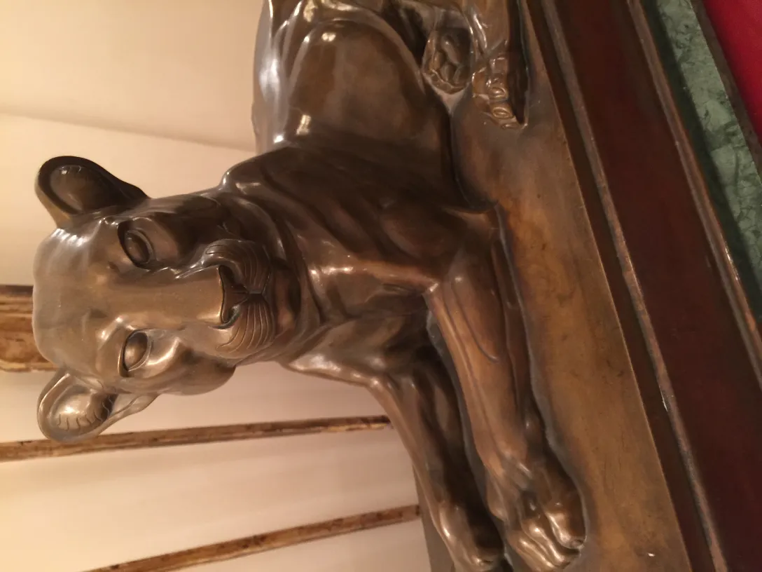 Escultura antiga de um leão em posição relaxada, detalhada.