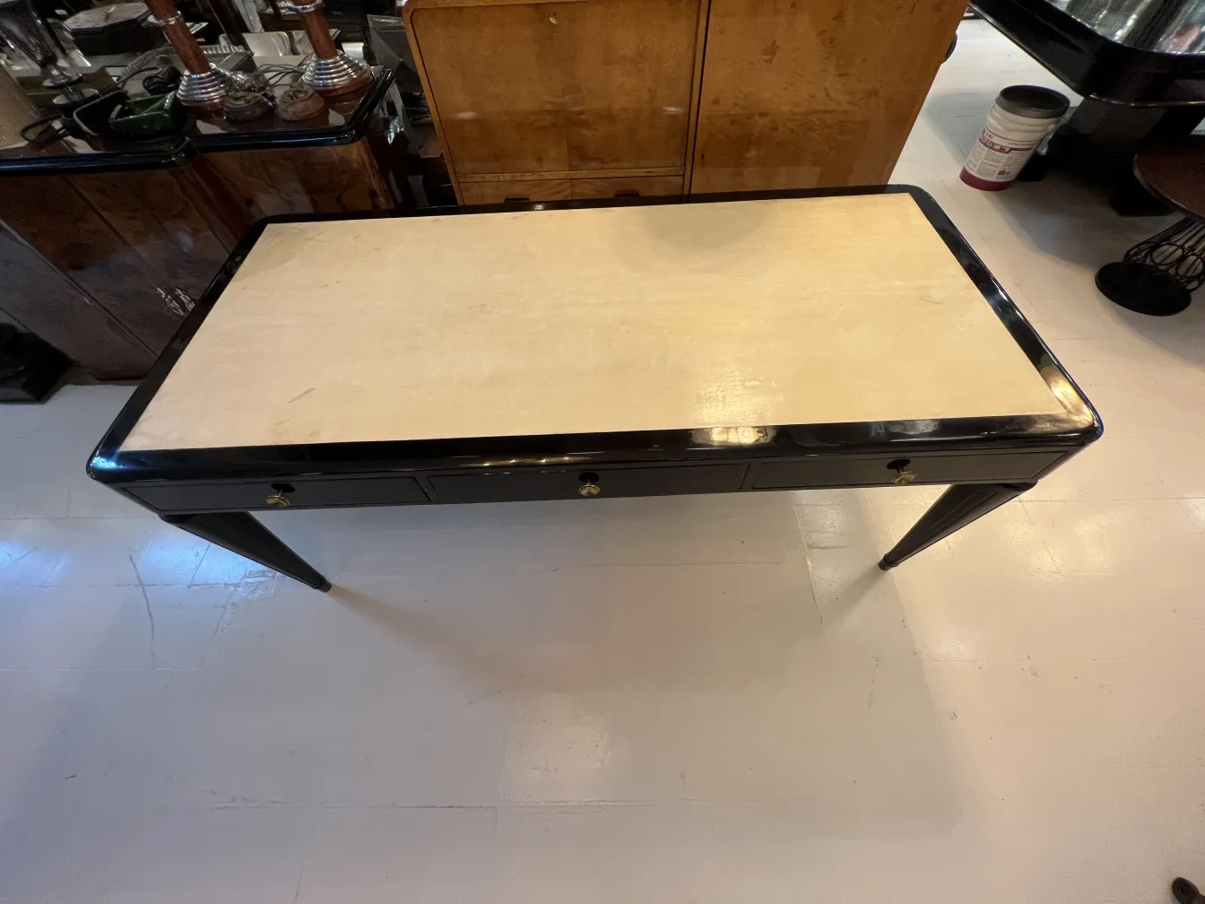 Escritorio antigo com topo claro e pernas elegantes, cercado por um ambiente clássico.