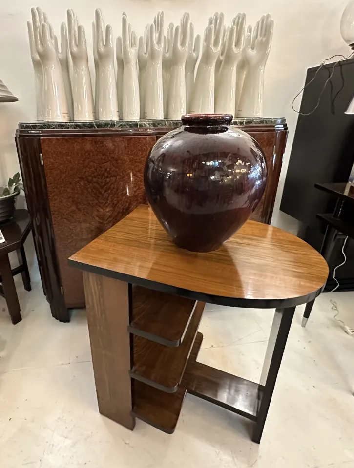 Dunkler antiker Keramikvase auf modernem Tisch, im Hintergrund weiße Keramikhände.