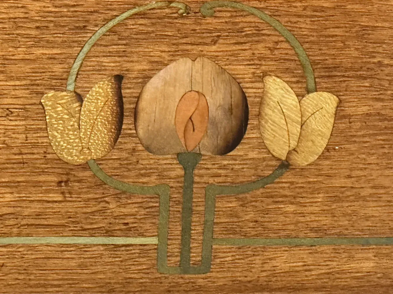Detail of an antique desk featuring leaf inlays in warm tones.