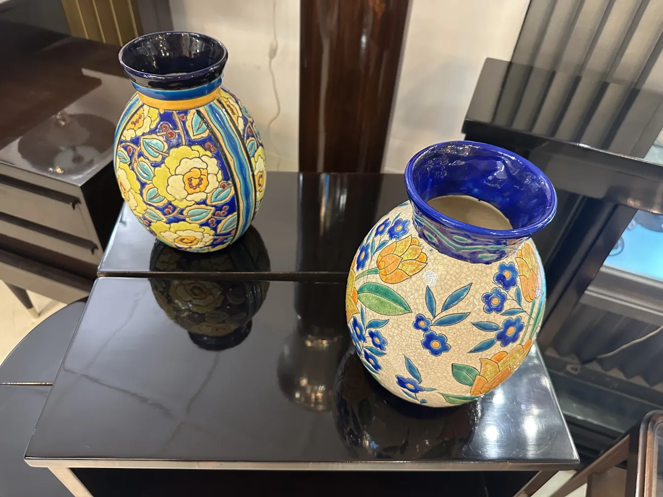 Due ceramiche antiche Boch Frères con motivi floreali vivaci, posizionate su una superficie lucida.