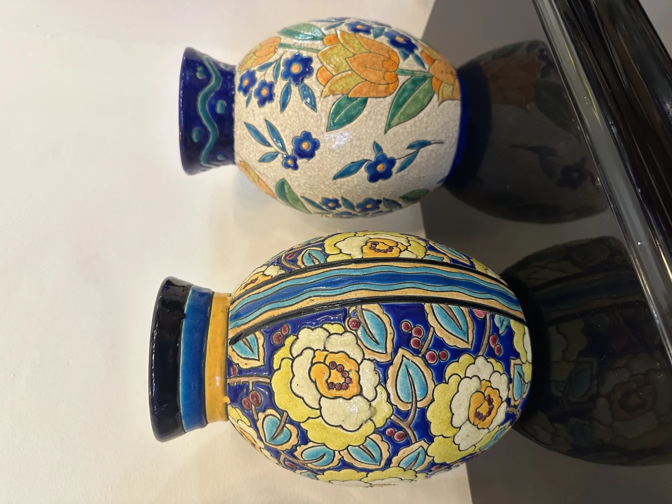 two antique ceramic vases featuring colorful floral designs on a reflective surface.