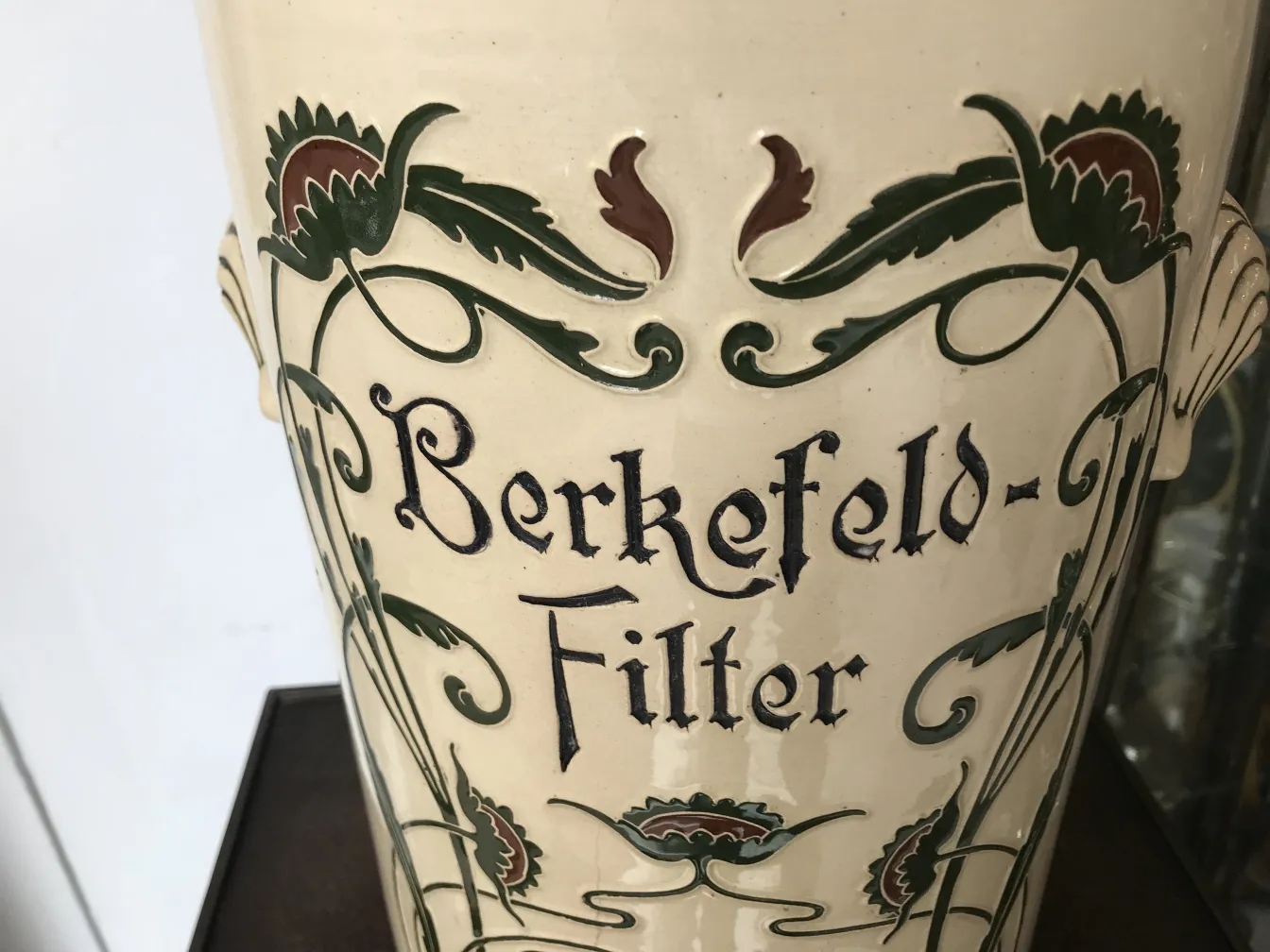 Antike Keramik mit hellen Hintergrund und floralem Design in Grün und Rot.