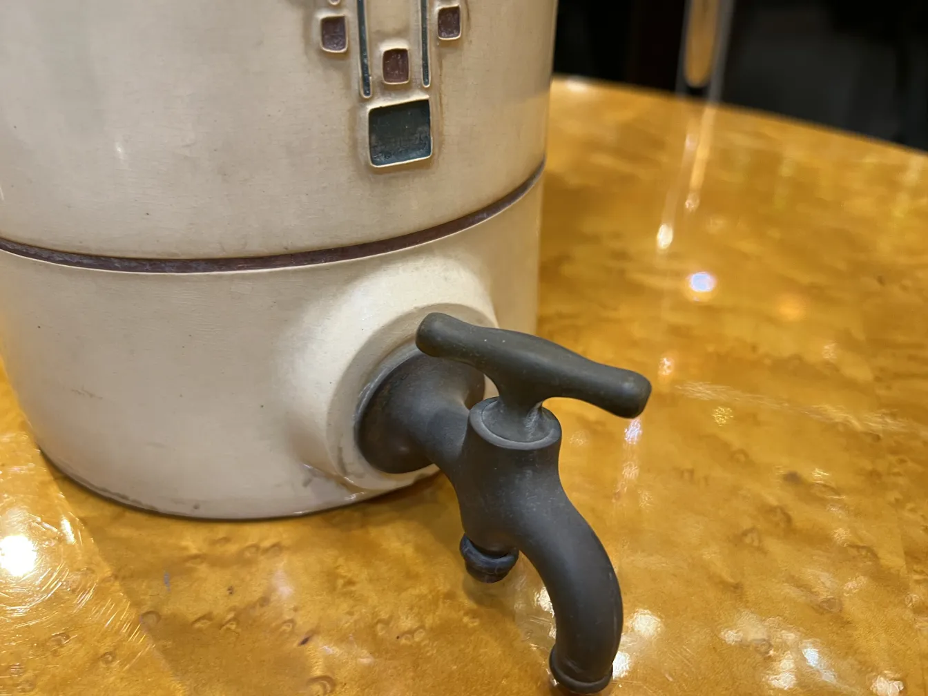 Ceramica antica dettagliata con rubinetto nero su tavolo lucido.