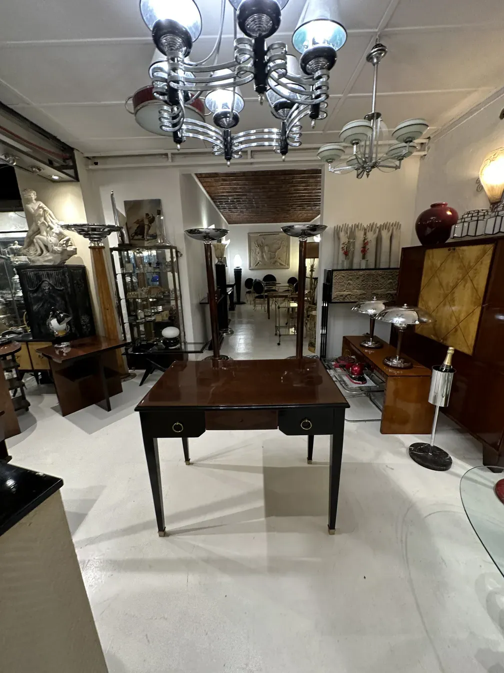 Bureau ancien avec surface sombre et poignées dorées, entouré d'objets décoratifs.