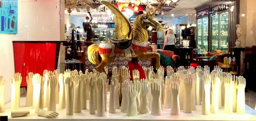 Vitrina con manos de cerámica blanca y un caballo dorado.