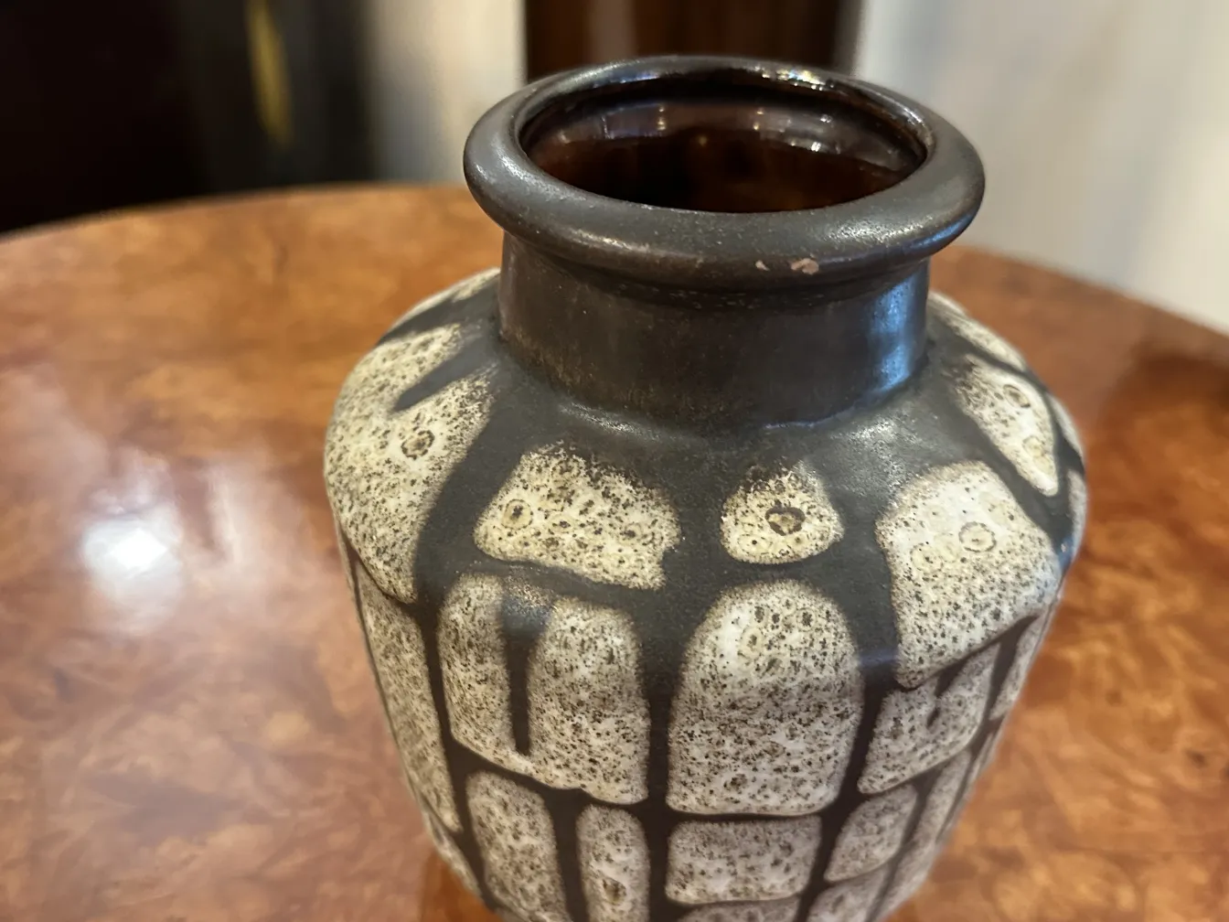Bouteille en céramique ancienne avec un design texturé en tons clairs et foncés sur une table en bois