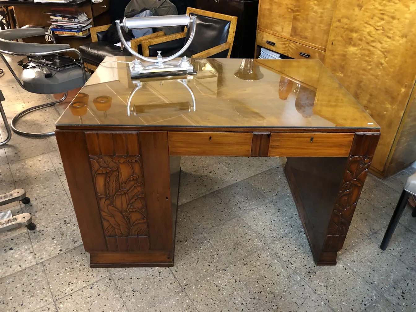 Escritorio antiguo de madera con detalles tallados y tapa de vidrio en un ambiente acogedor.