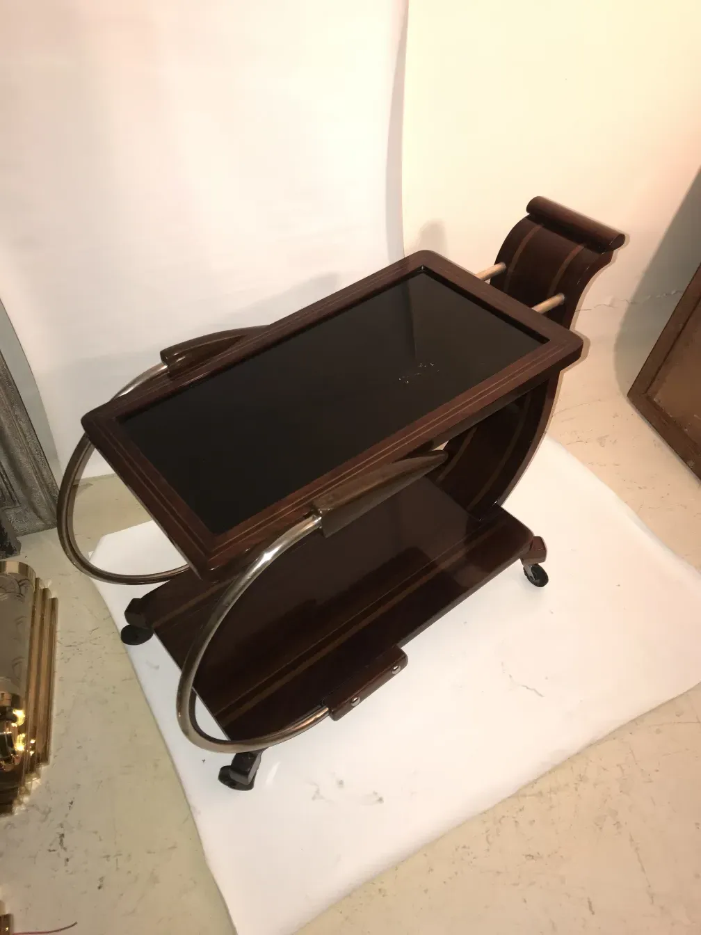 Mesa carrito antigua con superficie de cristal y ruedas, entorno minimalista.