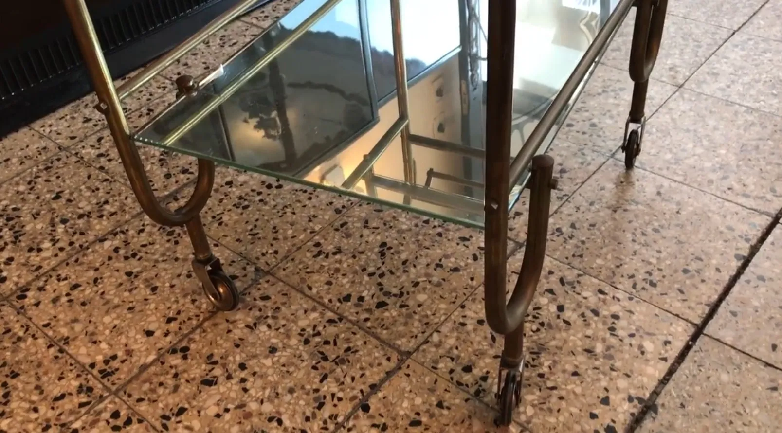 Mesa carrito antigua con ruedas y superficie de vidrio, ambiente elegante.